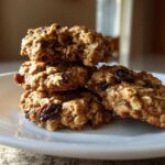 A stack of four soft, chewy oatmeal raisin cookies resting on a white plate.