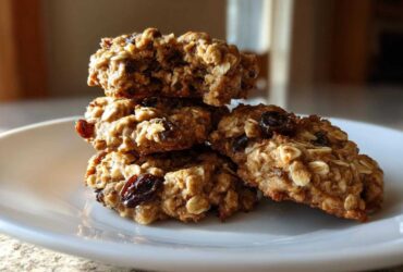 A stack of four soft, chewy oatmeal raisin cookies resting on a white plate.