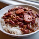 Close-up of a bowl of savory beans and rice topped with sliced smoked sausage.