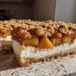 A close-up cross-section view of a rich peach cobbler cheesecake with a graham cracker crust and crumb topping.