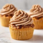 A close-up of one of the amazing pecan pie cupcakes, topped with a generous swirl of brown-spiced frosting.