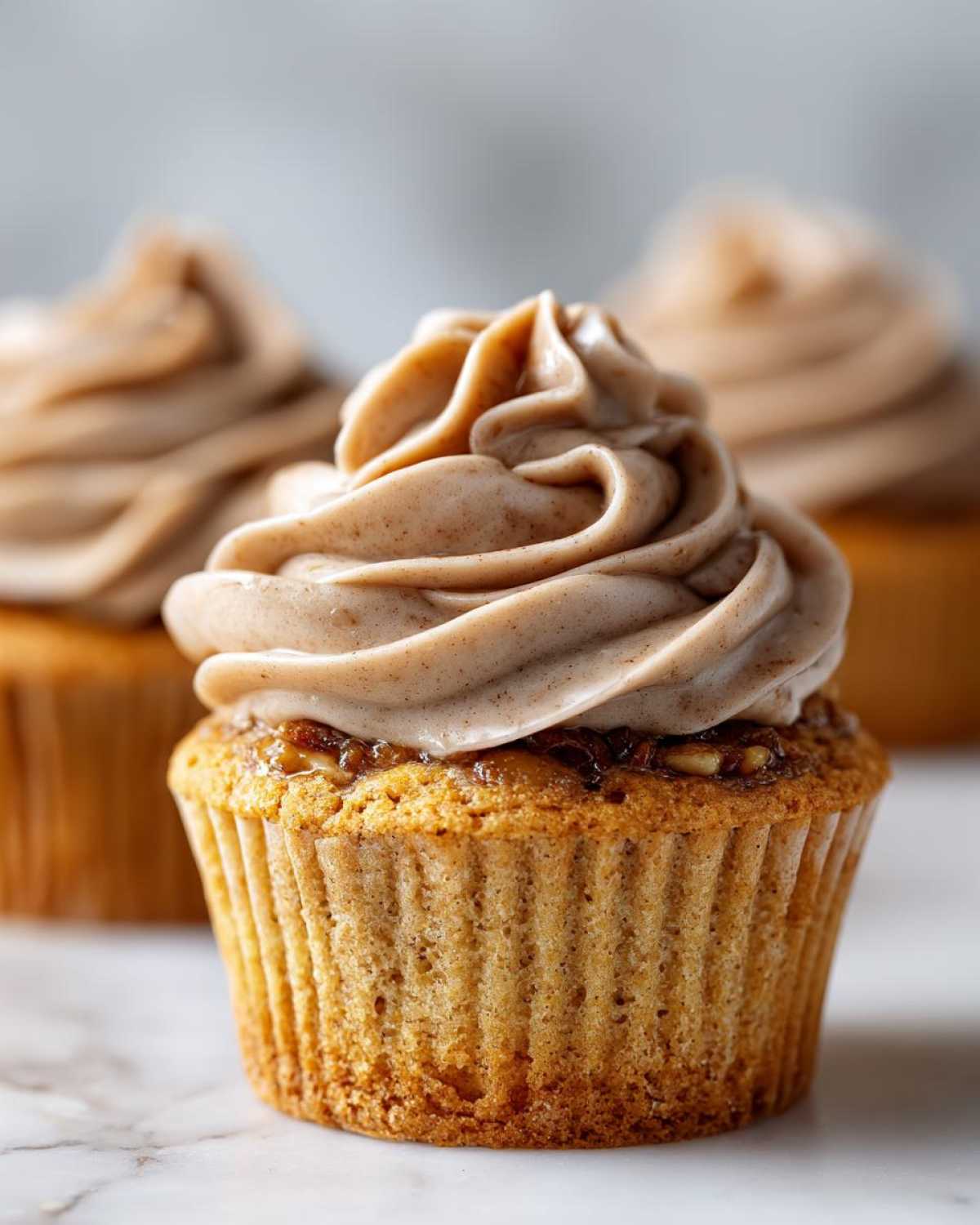 A close-up of one pecan pie cupcake topped with swirled, spiced frosting and pecan filling.