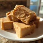 Close-up of several squares of rich, brown sugar penuche fudge stacked on a white plate.