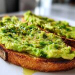 Close-up of two slices of avocado toast topped with mashed avocado, chives, and pepper.