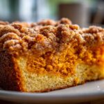 A close-up view of a moist slice of pumpkin crunch cake showing the orange pumpkin layer and crumb topping.
