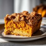 A close-up, appetizing slice of pumpkin crunch cake showing the bright orange pumpkin layer and crumbly topping.