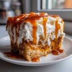 Close-up of a moist slice of pumpkin poke cake topped with whipped cream and dripping caramel sauce.