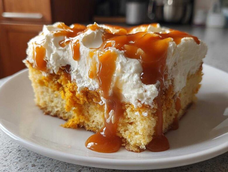 A close-up of a slice of moist pumpkin poke cake topped with whipped cream and drizzled heavily with caramel sauce.
