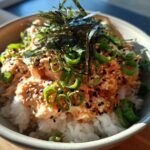 Close-up of a quick tuna rice bowl topped with spicy tuna mix, sesame seeds, green onions, and shredded nori.