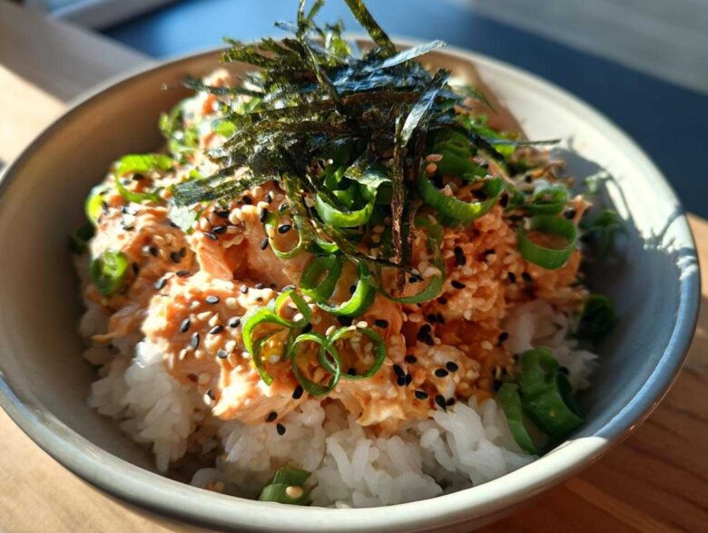 Close-up of a quick tuna rice bowl topped with spicy tuna mix, sesame seeds, green onions, and shredded nori.
