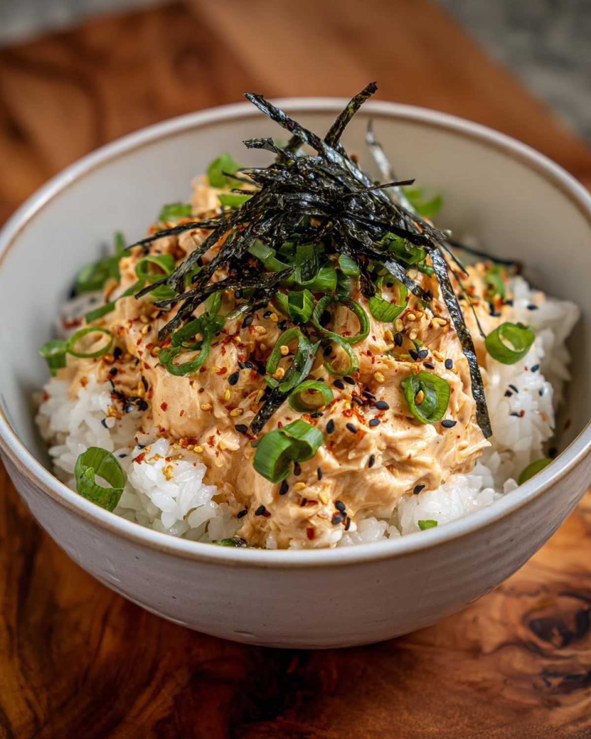 Close-up of a quick tuna rice bowl topped with creamy spicy tuna mixture, green onions, sesame seeds, and shredded nori.