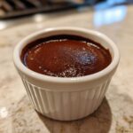 Close-up of rich, dark homemade chocolate pudding served in a small white fluted ramekin.