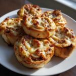 A plate of freshly baked sausage pinwheels topped with bubbly, melted, golden-brown cheese.