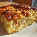 A thick, golden-brown slice of creamy scalloped potatoes and ham baked in a casserole dish.