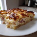 A close-up, appetizing slice of scalloped potatoes and ham with a golden, bubbly cheese crust on a white plate.