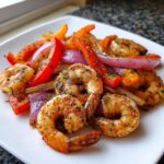 Close-up of seasoned shrimp fajitas with grilled red onion and bell peppers on a white plate.