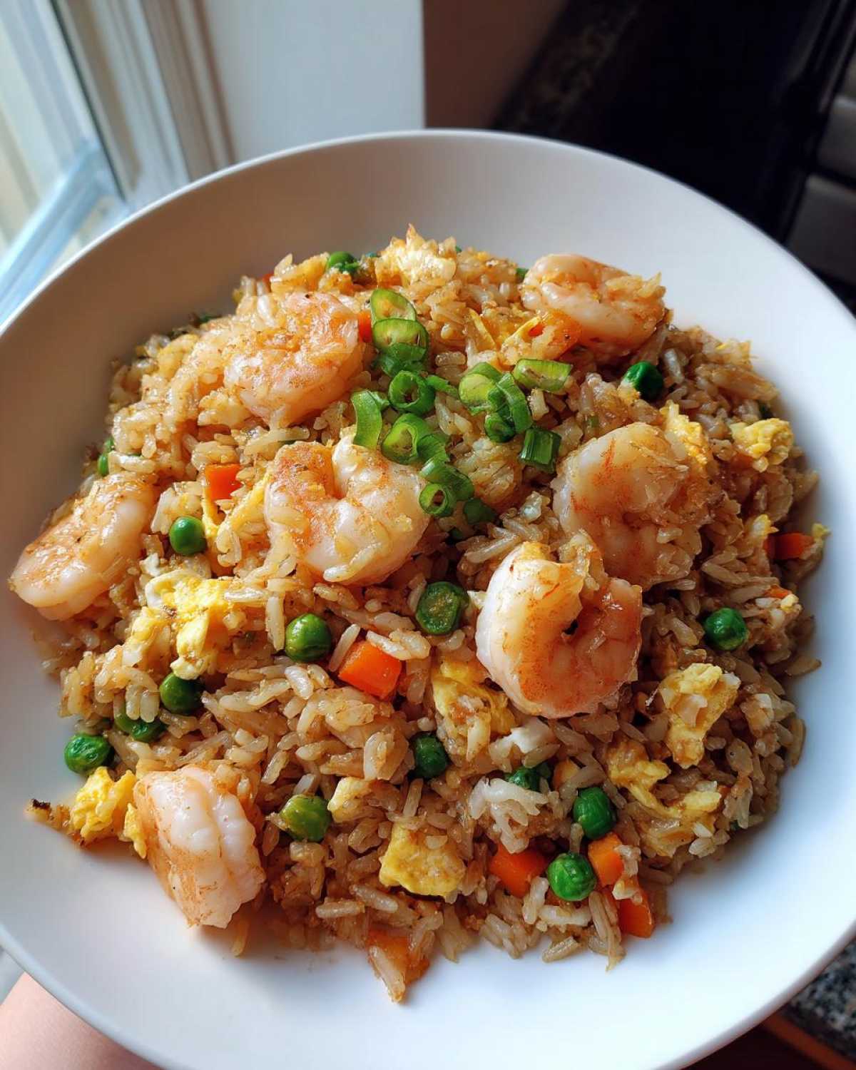 A close-up of a generous serving of shrimp fried rice recipe, topped with large shrimp and green onions.
