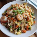 A bowl filled with finished shrimp fried rice recipe, featuring large shrimp, scrambled egg, peas, and carrots, topped with green onions.