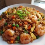 Close-up of a delicious shrimp fried rice recipe featuring large shrimp, peas, carrots, and scrambled egg, garnished with green onions.