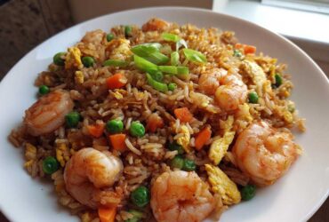 Close-up of a delicious shrimp fried rice recipe featuring large shrimp, peas, carrots, and scrambled egg, garnished with green onions.