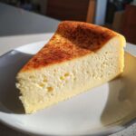 A thick slice of silky egg custard dessert dusted with cinnamon on a white plate.