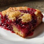 A close-up slice of warm cherry dump cake showing a bright red, gooey cherry filling and a golden crumb topping.