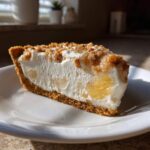 Close-up of a slice of creamy millionaire pie with a graham cracker crust and nut topping.