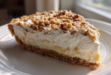 A generous slice of creamy millionaire pie featuring a graham cracker crust, thick filling, and crunchy nut topping.