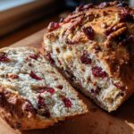 Close-up of a loaf of cranberry walnut bread, sliced to show the moist interior packed with dried cranberries and walnuts.