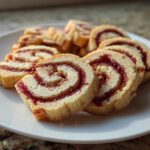 Close-up of several sliced pinwheel cookies arranged on a white plate, showing the swirl of jam filling.