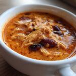 Close-up of a white bowl filled with rich, orange-red slow cooker buffalo chicken chili featuring shredded chicken and kidney beans.