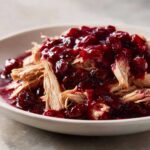 Shredded slow cooker cranberry chicken topped generously with rich, dark red cranberry sauce.