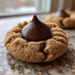 A close-up of a soft, sugar-coated peanut butter blossom cookie topped with a milk chocolate kiss.