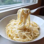 A fork lifting spaghetti coated in creamy olive garden alfredo sauce from a white bowl.