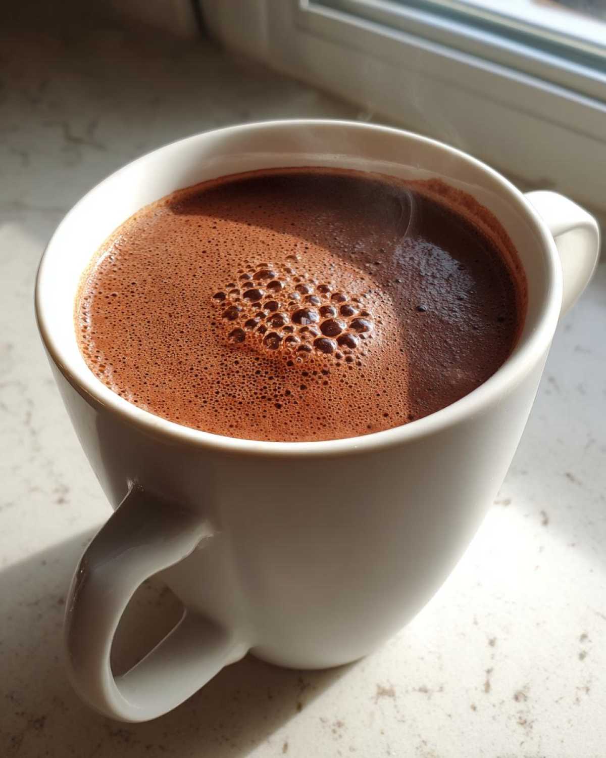 Close-up of a steaming white mug filled with rich, foamy crockpot hot chocolate recipe.