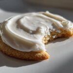 Close-up of a soft sugar cookie topped with thick, creamy white sugar cookie icing recipe, with a bite taken out.