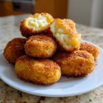 A stack of golden brown, crispy potato croquettes, with one cut open revealing the creamy interior.