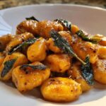 Close-up of vibrant orange sweet potato gnocchi tossed in brown butter sauce with crispy sage leaves.