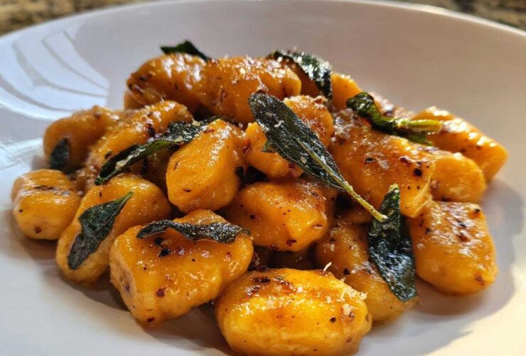 Close-up of vibrant orange sweet potato gnocchi tossed in brown butter sauce with crispy sage leaves.