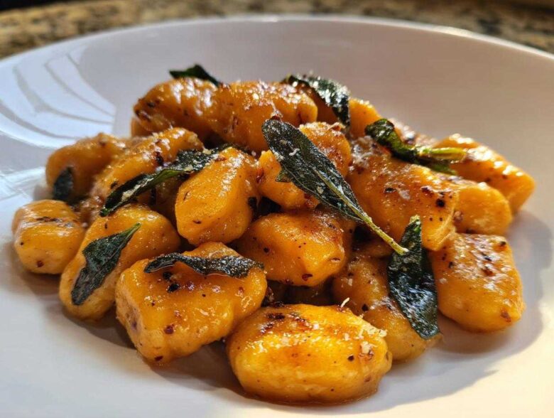 Close-up of vibrant orange sweet potato gnocchi tossed in brown butter sauce with crispy sage leaves.