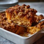 A spoonful lifts a moist slice of sweet potato souffle topped with a crunchy pecan streusel from a white baking dish.