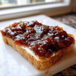 A slice of toasted bread generously topped with thick, dark homemade apple butter spread.