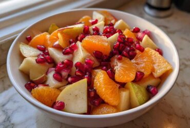 Close-up of a white bowl filled with a colorful winter fruit salad featuring orange segments, diced pears, and bright red pomegranate seeds.