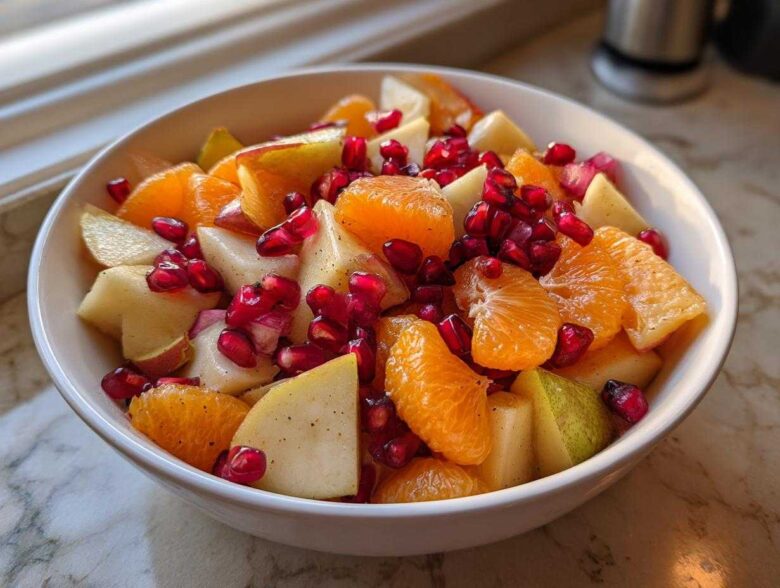 Close-up of a white bowl filled with a colorful winter fruit salad featuring orange segments, diced pears, and bright red pomegranate seeds.