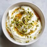 Close-up overhead view of creamy whipped goat cheese topped with chopped pistachios and a drizzle of honey.