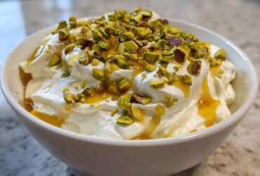 A white bowl filled with creamy whipped goat cheese, drizzled with honey and topped with chopped pistachios.