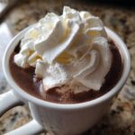 Close-up of a rich, dark chocolate drink topped generously with fluffy white whipped cream, perfect for whipped hot chocolate.