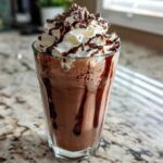 A tall glass filled with rich, blended frozen hot chocolate topped with whipped cream and chocolate shavings.
