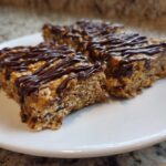 Three homemade protein bars with oats and a rich chocolate drizzle served on a white plate.