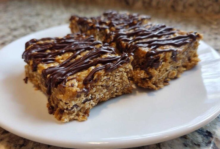 Three homemade protein bars with oats and a rich chocolate drizzle served on a white plate.